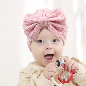 Close-up of pink knitted baby turban hat featuring a large bow and ribbed texture fabric