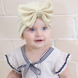 Detail of baby turban hat in beige waffle knit fabric featuring a large decorative bow