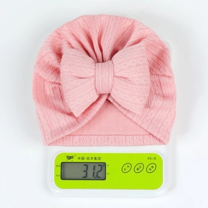 Pink newborn baby hat with large stuffed bow weighing 31.2 grams on a scale