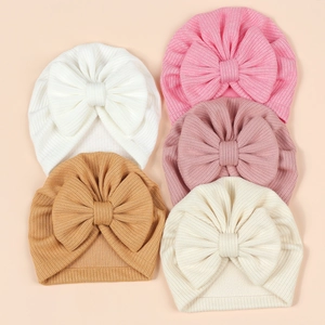 Flat lay of five soft ribbed knit baby hats with oversized bows in various neutral colors