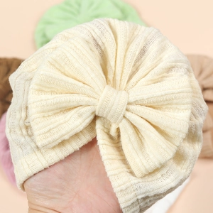Beige baby turban hat featuring a large soft knit bow and vertical ribbed texture