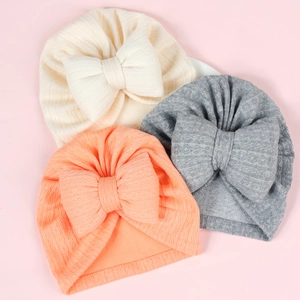 Close-up of three newborn headwraps in cream, grey, and orange with large bows