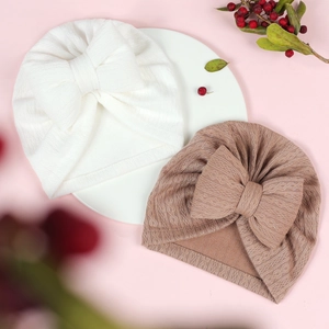 Close-up of baby turban hats with large bows in white and brown textured knit