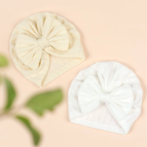 Detailed view of two baby knot hats in beige and white ribbed knit with large bows