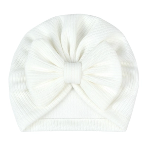 Detail of white striped knit infant turban hat with large decorative bow on white background