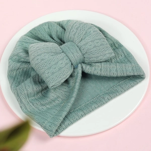 Morandi teal baby turban hat with a large soft bow on a white display plate