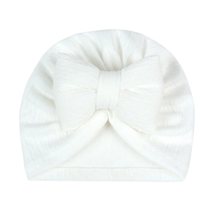 Close-up of white knitted newborn turban hat with a large decorative bow detail