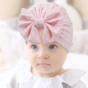 Close-up of baby girl wearing a pale pink turban hat with a large decorative bow