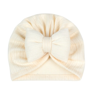 Detailed close-up of cream beige infant turban hat with large bow and ribbed knit texture