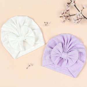 Detail of white and lavender baby turban hats with large bows and ribbed knit fabric texture