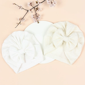 Detailed close-up of white baby turban hats with large bows on a neutral background