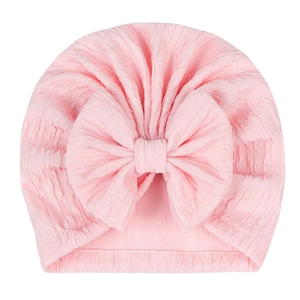 Pink infant turban hat with a large bow detail and soft pleated texture on white background