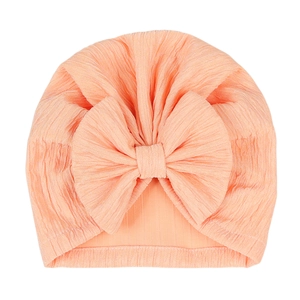 Detail view of the soft orange-pink baby turban hat with large bow and pleated texture