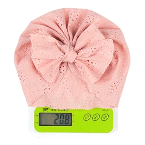 Détail d'un bonnet en dentelle rose pour bébé avec nœud pesant 20,8 g sur balance