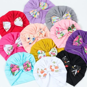 Turbans colorés pour bébés avec nœuds imprimés disposés sur un fond blanc épuré