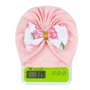 Pink infant turban hat with large bow weighing approximately 33.9g on a digital scale
