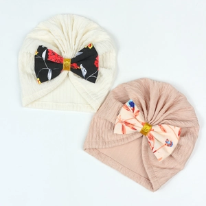 Detail showing two knit baby turban hats in cream and pink with large glittery bows