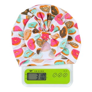 Baby-Mütze mit Blumenmuster und großer Donut-Schleife auf einer digitalen Waage