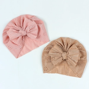 Détail de bonnets turban ajourés pour bébé avec grands nœuds en rose et beige