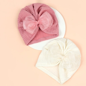 Close-up of baby turban hats with large organza bows in pink and beige colors