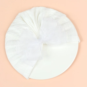 Detailed view of white pleated baby turban hat with a large mesh bow on a flat surface