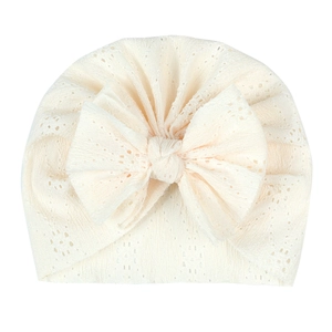 Détail du bonnet pour bébé en dentelle ajourée blanc crème avec un grand nœud décoratif