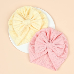 Détail du tissu gaufré et des grands nœuds sur les bonnets de bébé rose et jaune