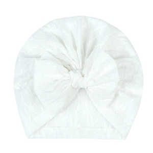Close-up of white baby lace turban hat featuring a large decorative bow and floral texture