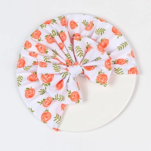 Detail einer floralen Baby-Turbanmütze mit großer Schleife und orangefarbenem Rosenmuster