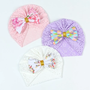 Close-up of three breathable newborn beanies with floral printed bows and golden details