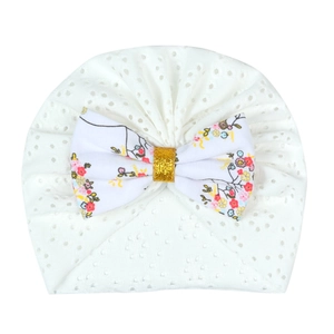 Detail of white newborn baby hat with floral bow and breathable eyelet fabric texture