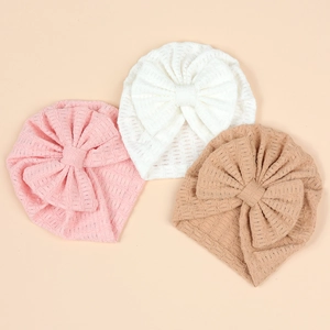 Détail de trois bonnets bébé en tricot gaufré blanc, rose et beige avec grands nœuds