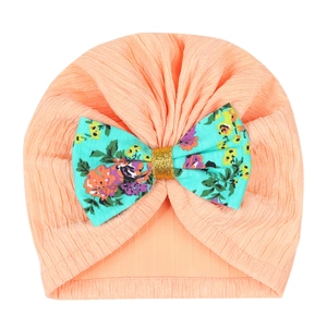 Detail of baby turban hat in peach knit cotton with a large floral bow and gold sequins