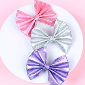 Detail of three glossy laser-textured bow hair clips in pink, silver and purple colors