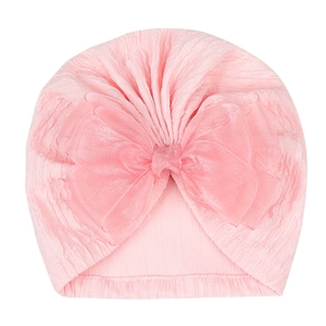Detail of baby pink knit beanie featuring a large soft bow on a white background