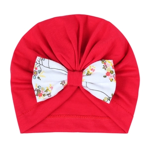 Détail du turban rouge pour bébé avec un grand nœud blanc à motifs floraux doux