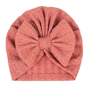 Détail du bonnet à nœud pour bébé montrant la texture gaufrée en rose poudré délicat