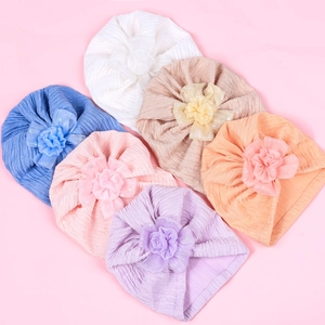 Flat lay of six baby turban hats with large flower details in varied soft colors
