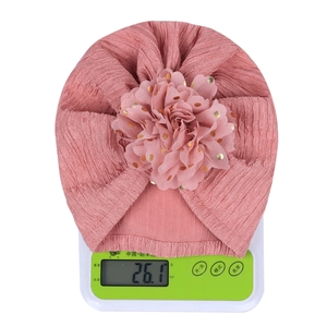 Pink infant turban hat with large gold-dot flower shown weighing 26.1g on a scale