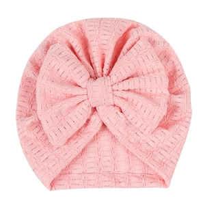Détail du bonnet pour nouveau-né en maille gaufrée rose avec un grand nœud décoratif