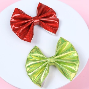 Detail of red and teal shiny leather bow hair clips with textured finish on a pink base