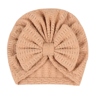 Gros plan d'un bonnet turban beige pour nouveau-né avec un nœud gaufré et tissu plissé