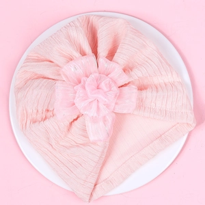 Detail of baby pink turban hat featuring a large layered flower and ribbed knit texture
