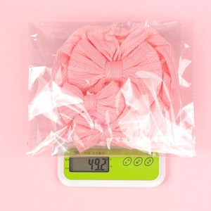Baby pink knitted headband set with bows being weighed on a scale showing 49g