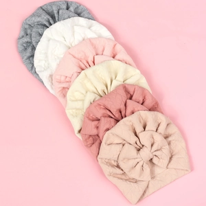 Set of six knit baby turbans with large bows in neutral colors on a pink background