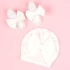 Flat lay of white baby turban hat and matching soft booties with oversized bows