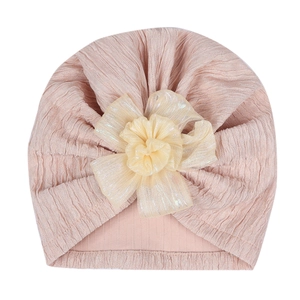 Detail of baby turban hat featuring a peach jacquard fabric and large layered mesh flower