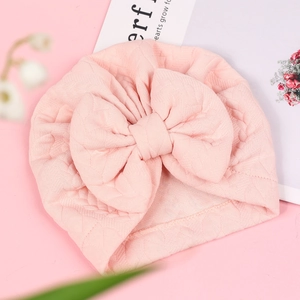 Detail of pink knitted baby turban hat with oversized bow and diamond texture pattern
