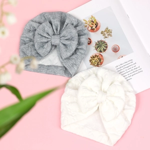 Detailed view of knitted grey and white baby turban hats with large soft decorative bows