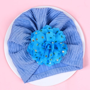 Detail of baby blue turban hat with large gold-spotted chiffon flower on soft fabric